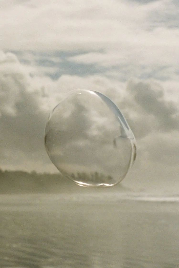 A clear sphere of water resting on a misty shoreline